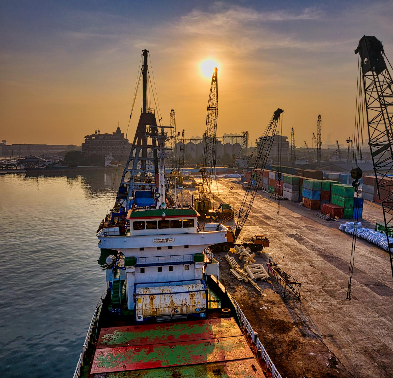 A vibrant scene of cargo operations during sunrise at a busy port in Indonesia.